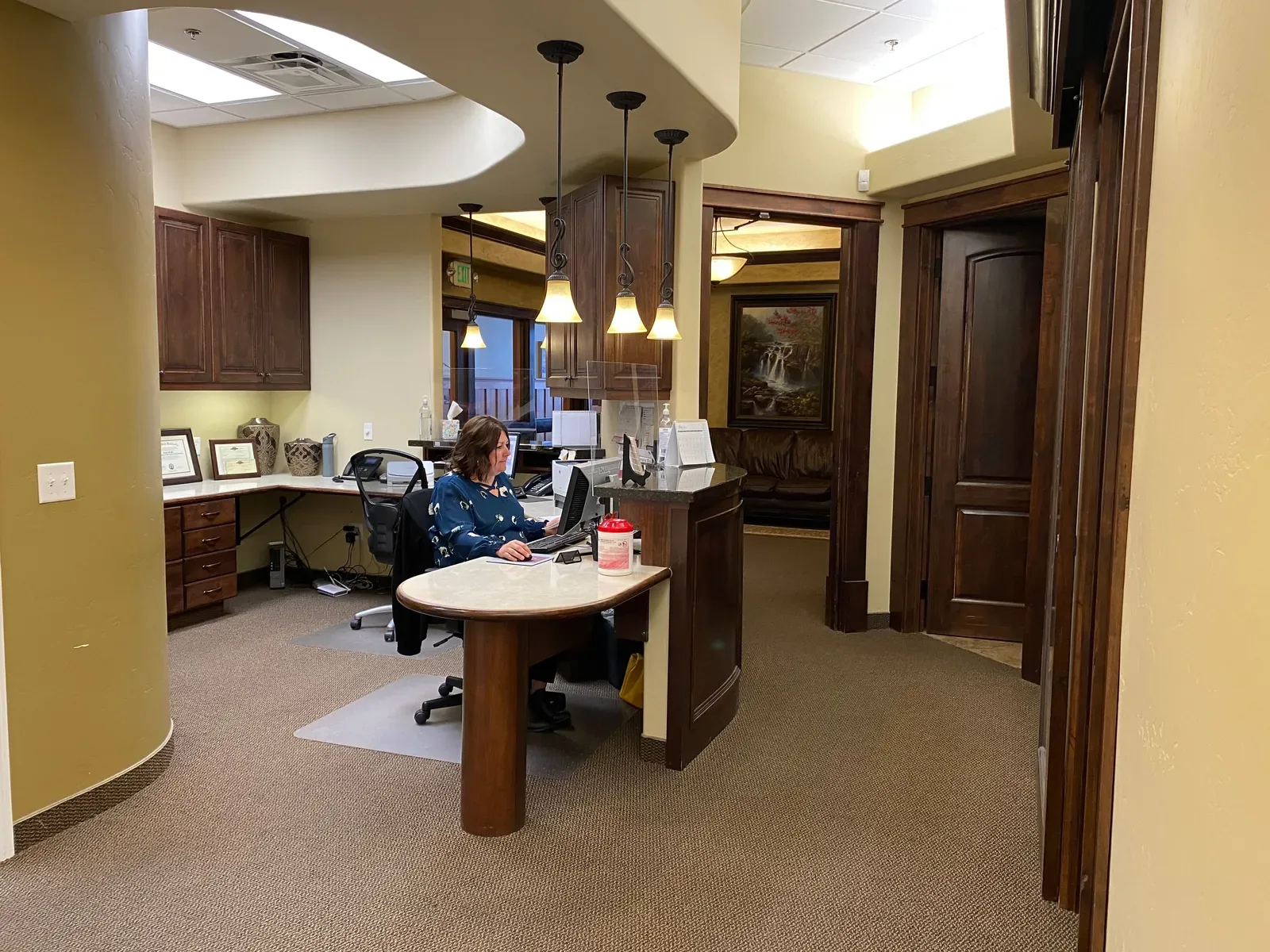 Receptionist seated at a computer behind a curved counter in an office reception area.